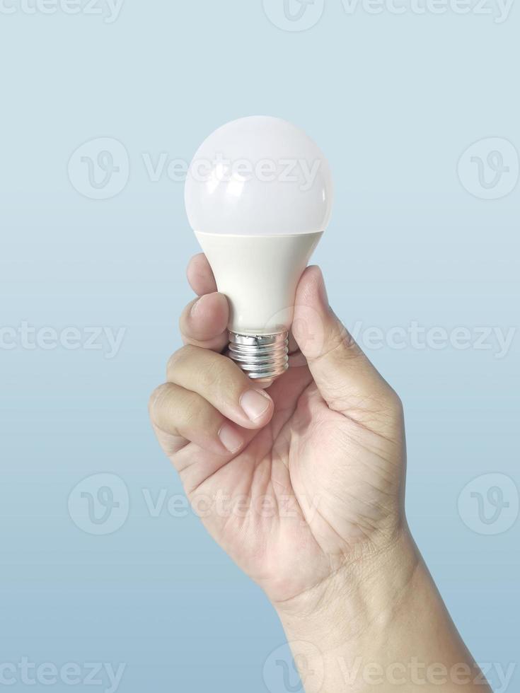 Hand, die eine LED-Glühbirne auf blauem Hintergrund hält. mit wirtschaftlichem und umweltfreundlichem Glühbirnenkonzept. Idee. Energiesparlampe in der Hand der Frau foto
