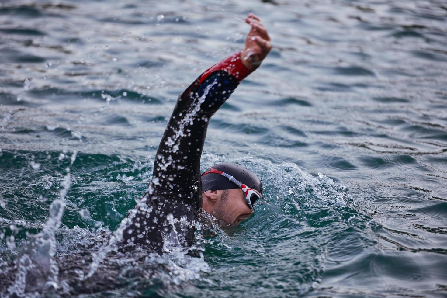 Triathlon-Athlet, der bei Sonnenaufgang auf dem See schwimmt und einen Neoprenanzug trägt foto