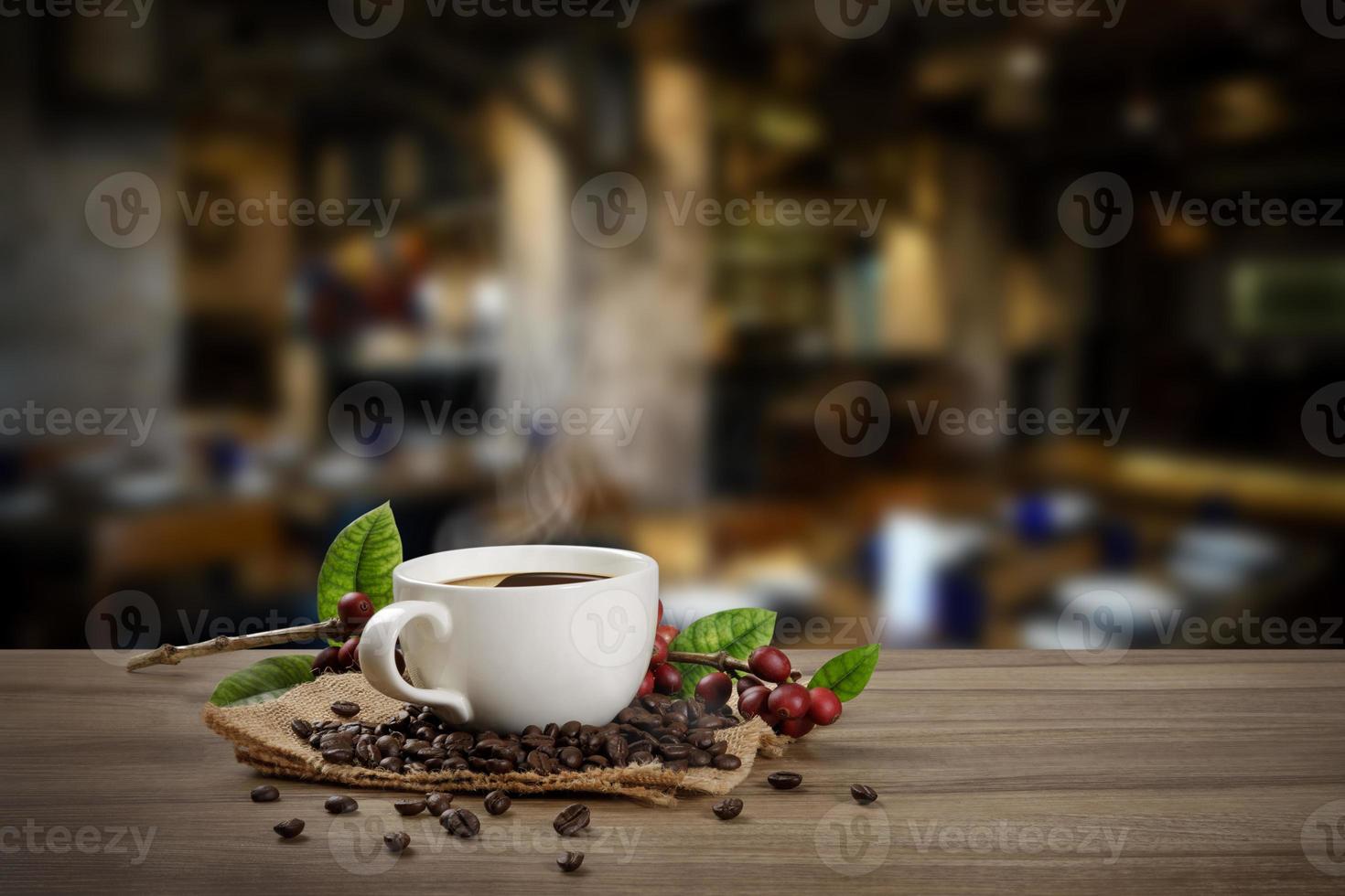 Heiße Kaffeetasse mit frischen organischen roten Kaffeebohnen und Kaffeeröstungen auf dem Holztisch im Hintergrund des Cafés foto