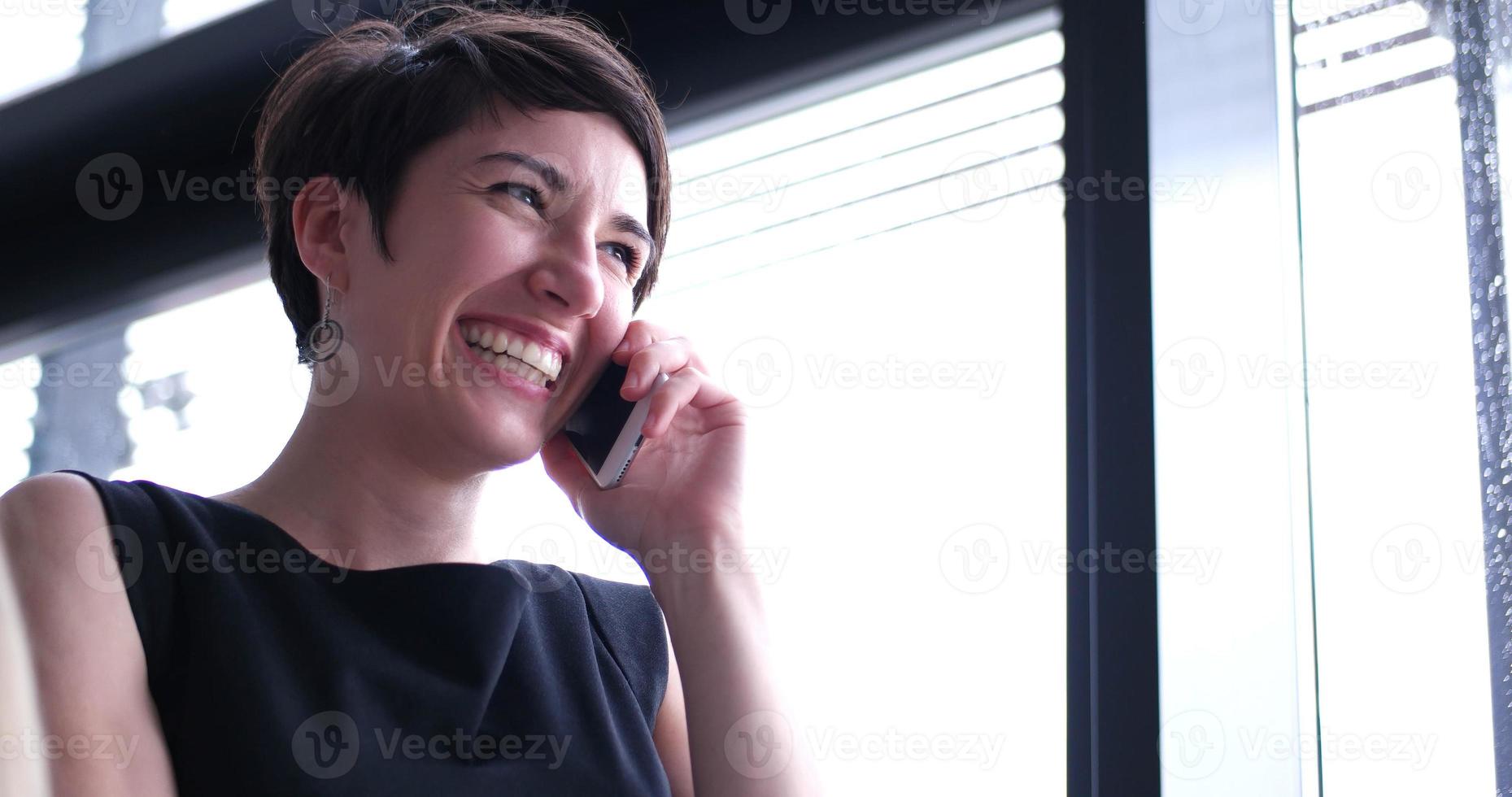 Geschäftsmädchen, das in einem modernen Gebäude in der Nähe des Fensters mit Telefon steht foto