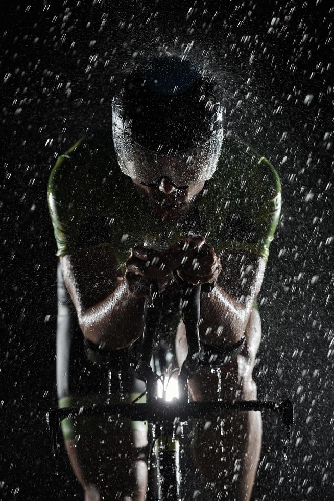 Triathlon-Athlet, der in regnerischer Nacht schnell Fahrrad fährt foto