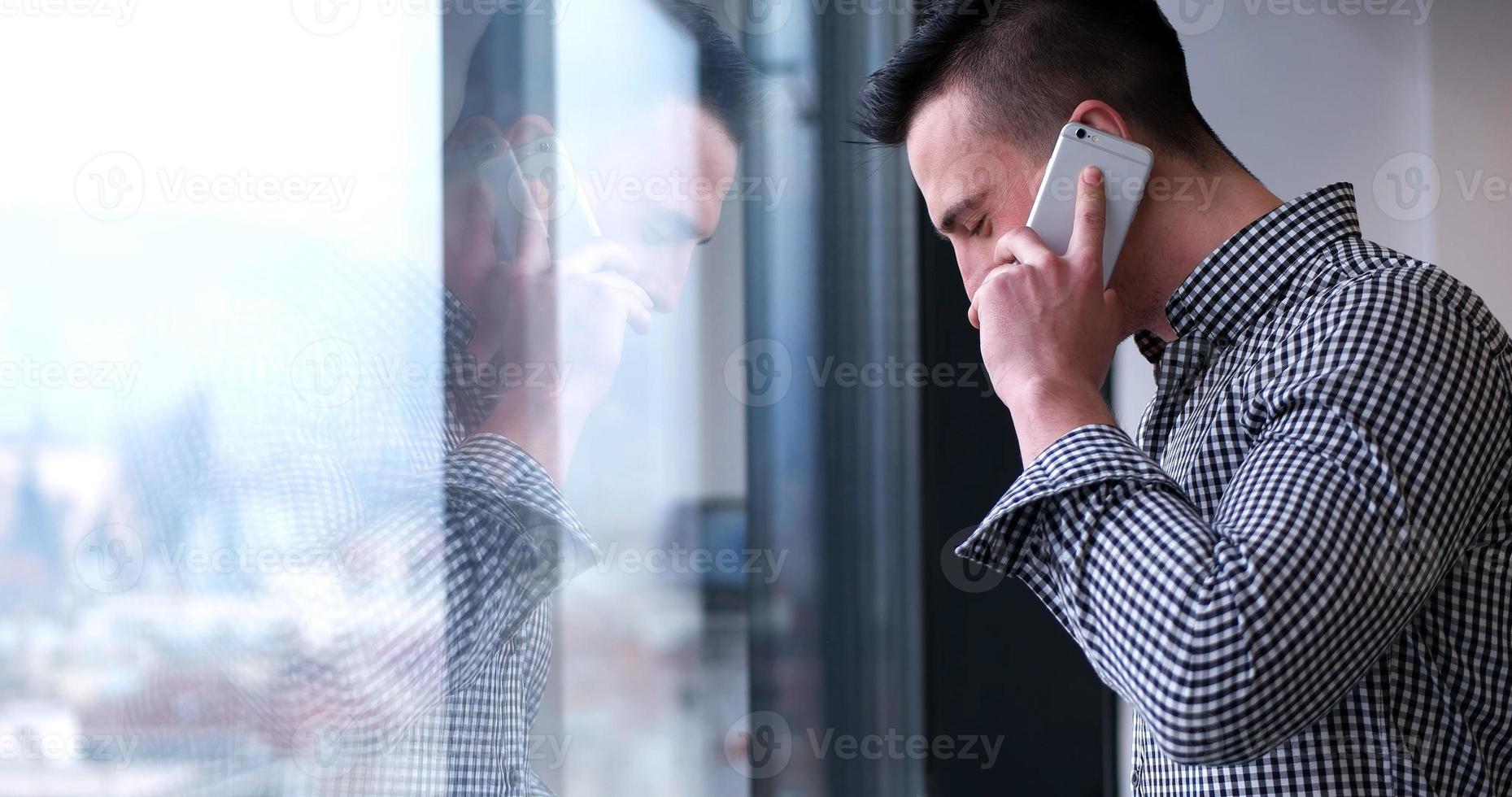 Geschäftsmann, der am Handy spricht und aus dem Bürofenster schaut foto