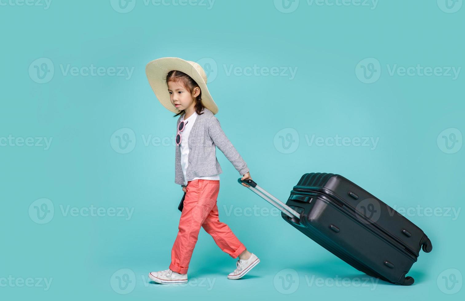 asiatische Touristenfrau des kleinen Mädchens mit schwarzem Gepäck, um an den Wochenenden zu reisen, leerer Raum in der Atelieraufnahme lokalisiert auf buntem blauem Hintergrund foto
