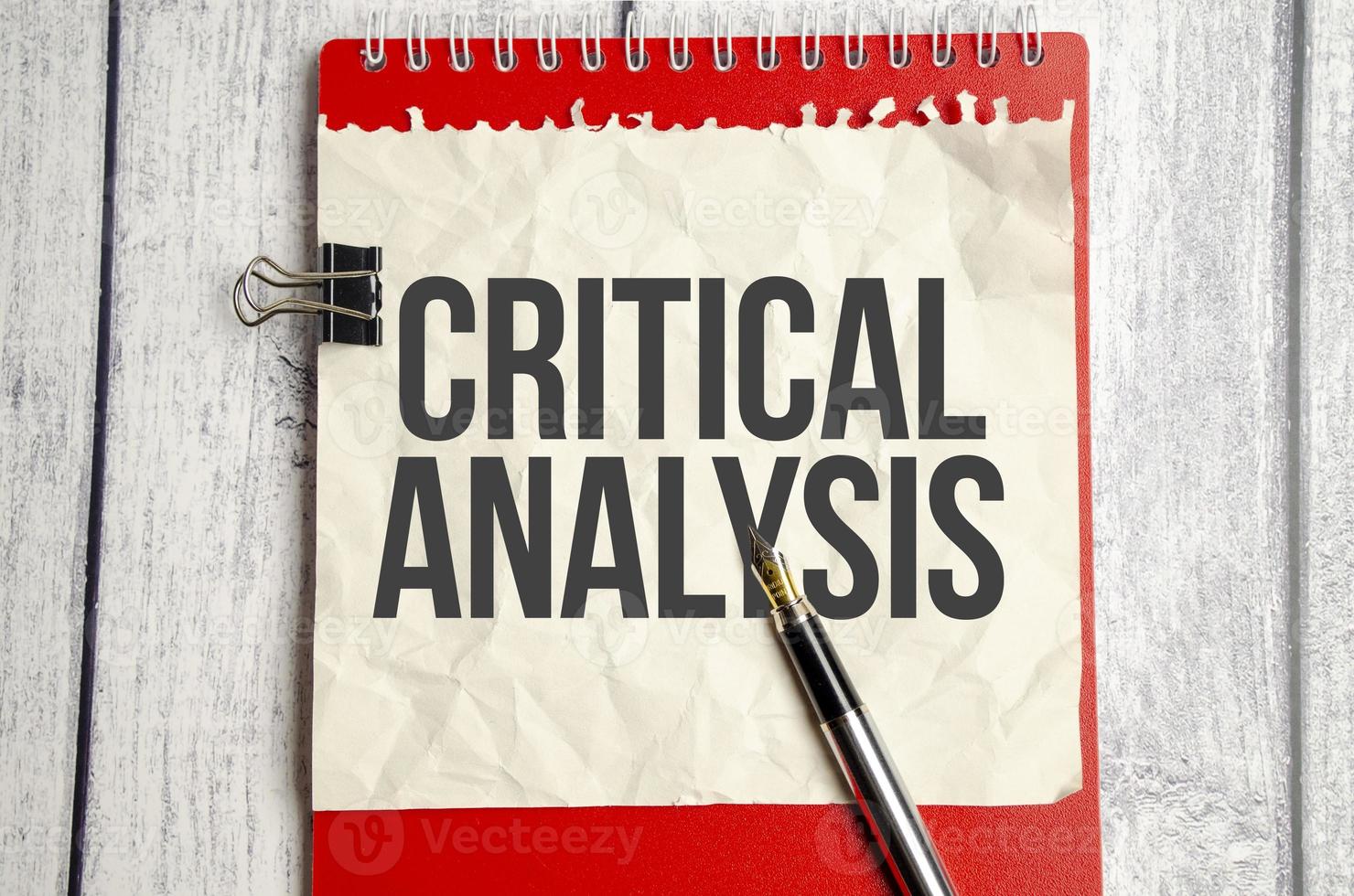 Kritische Analyse, Text auf weißem Papier und rotem Notizblock auf Holzhintergrund foto