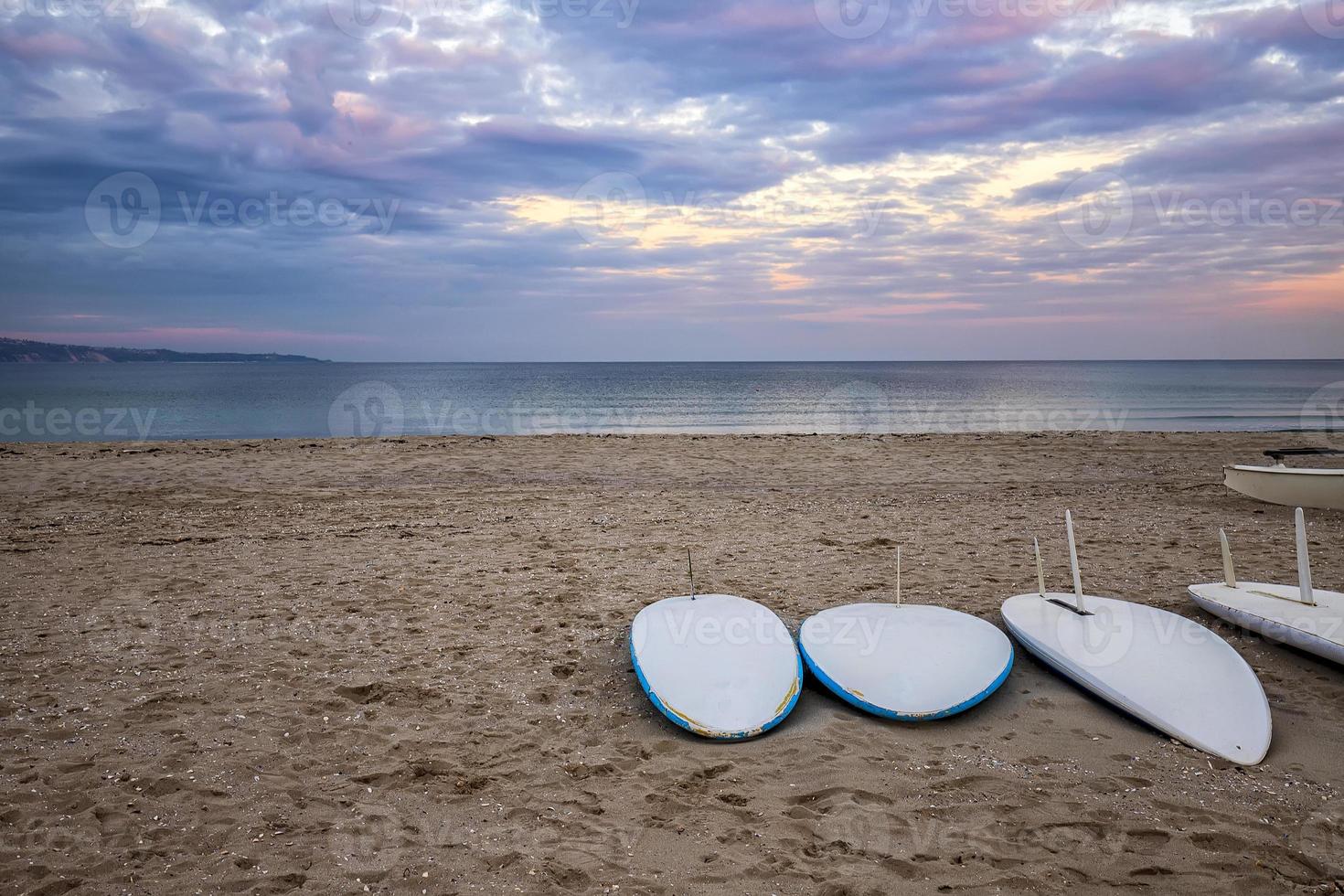 Einige Surfbretter am Strand an einer Küste bei Sonnenuntergang mit schönen Wolken. Wassersport Hintergrund foto