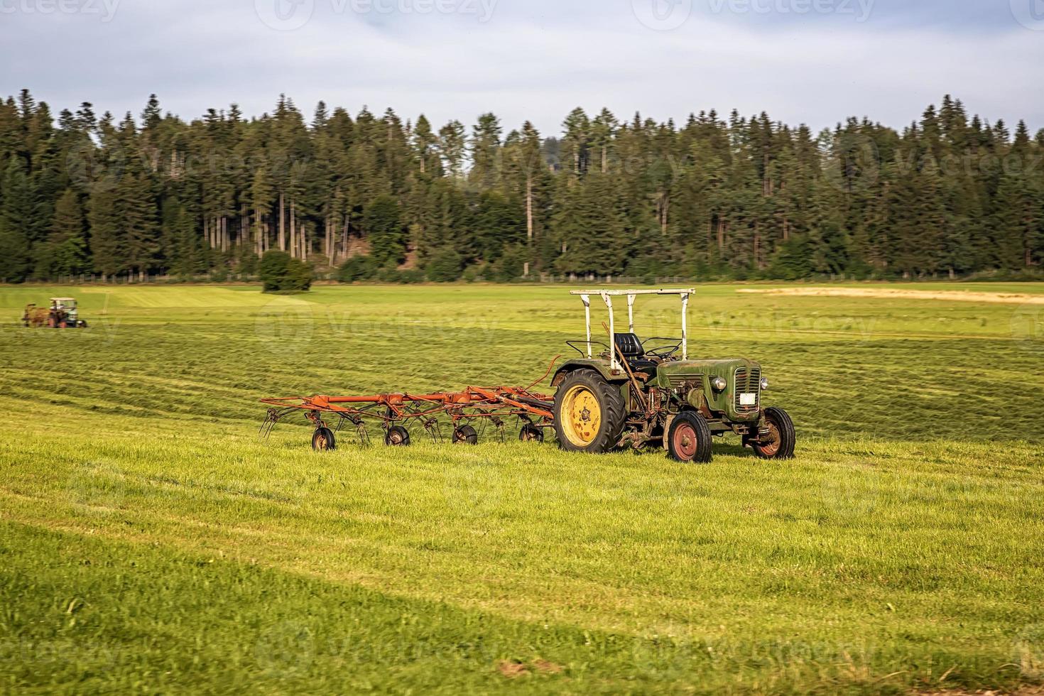 Landmaschinen, ein Traktor, der Gras auf einem Feld vor blauem Himmel sammelt. Saisonernte, Gras, landwirtschaftliche Flächen. selektiver Fokus foto