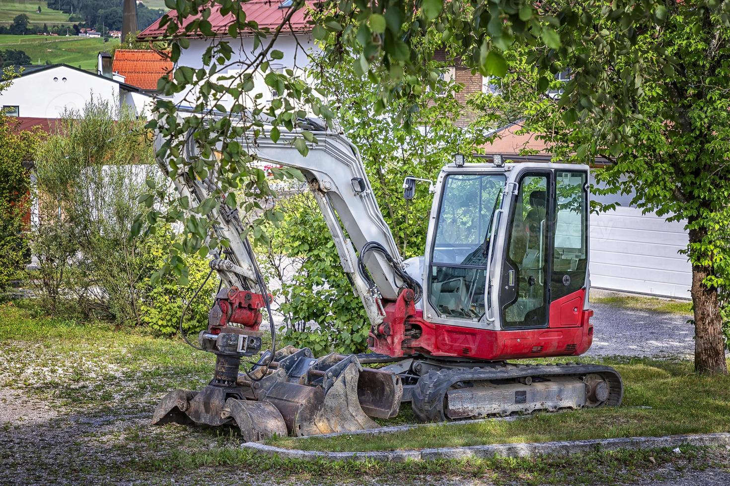 Kleiner angehaltener Bagger mit einer Schaufel, die unter einem Baum geparkt ist foto