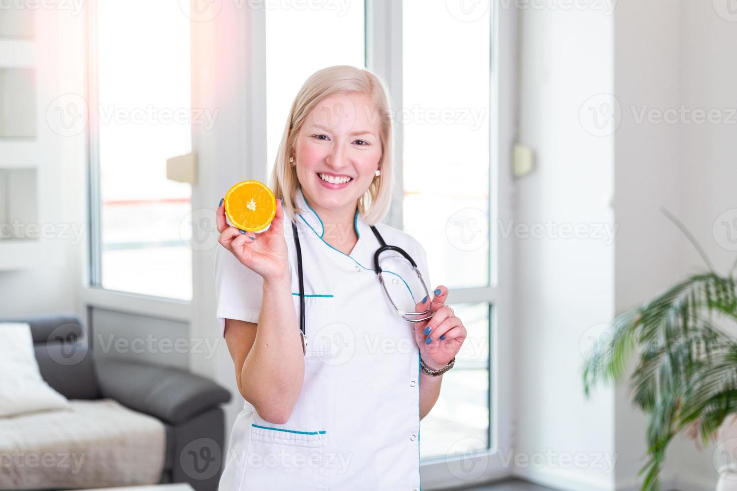 Die lächelnde Ernährungsberaterin in ihrem Büro hält eine Orangenfrucht und zeigt gesundes Gemüse und Obst, Gesundheits- und Ernährungskonzept. Ernährungsberaterin mit Früchten foto