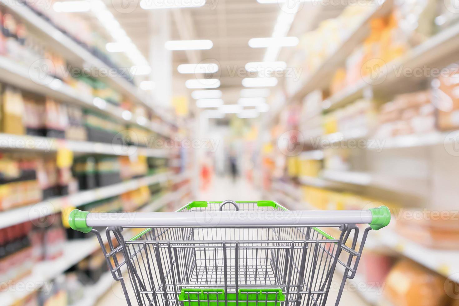 leerer grüner Einkaufswagen mit abstraktem, unscharfem Supermarkt-Discounter-Gang und Würzsaucen-Produktflaschenregalen mit defokussiertem Hintergrund foto