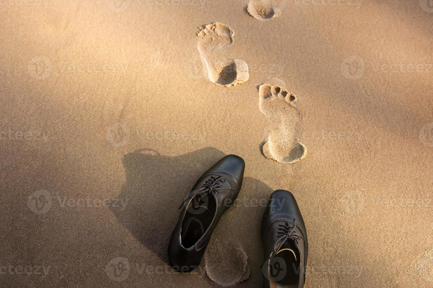 work-life-balance-konzept, geschäftsmann zieht seine arbeitenden oxford-schuhe aus und lässt sie an einem sonnigen tag am sandstrand für einen spaziergang ins meer. Ansicht von oben foto