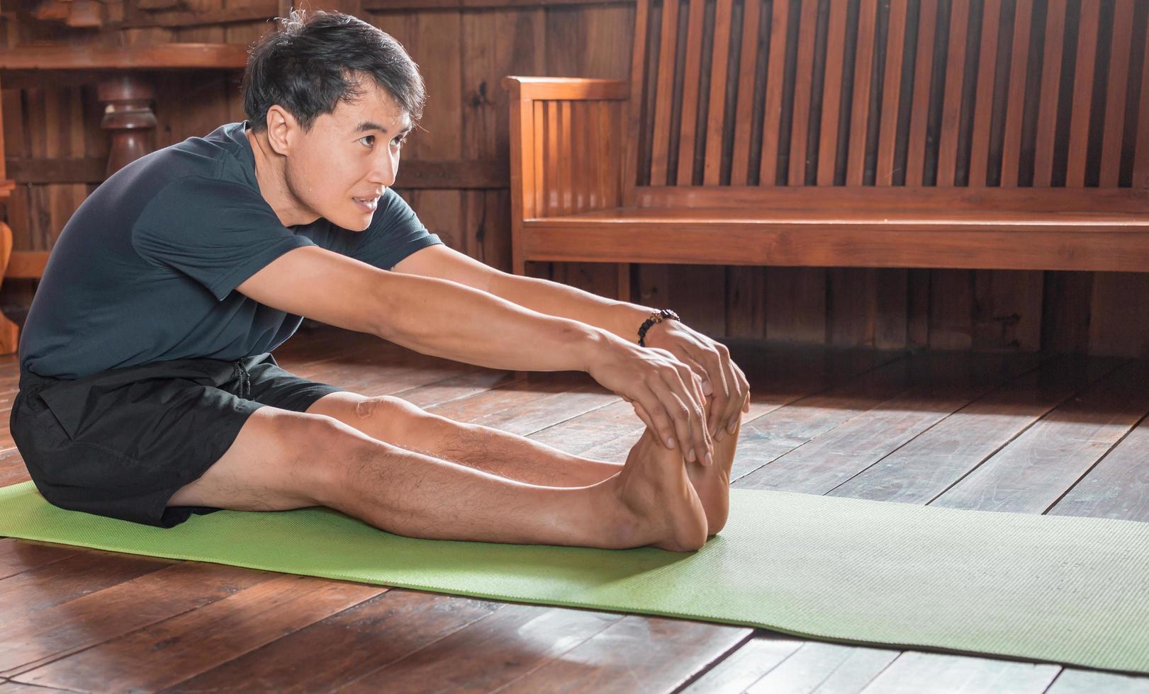 sportlicher asiatischer mann in schwarz macht yoga, während er zu hause auf yogamatte mit holzboden trainiert. mann yoga praxis pose training gesundes lebenskonzept foto