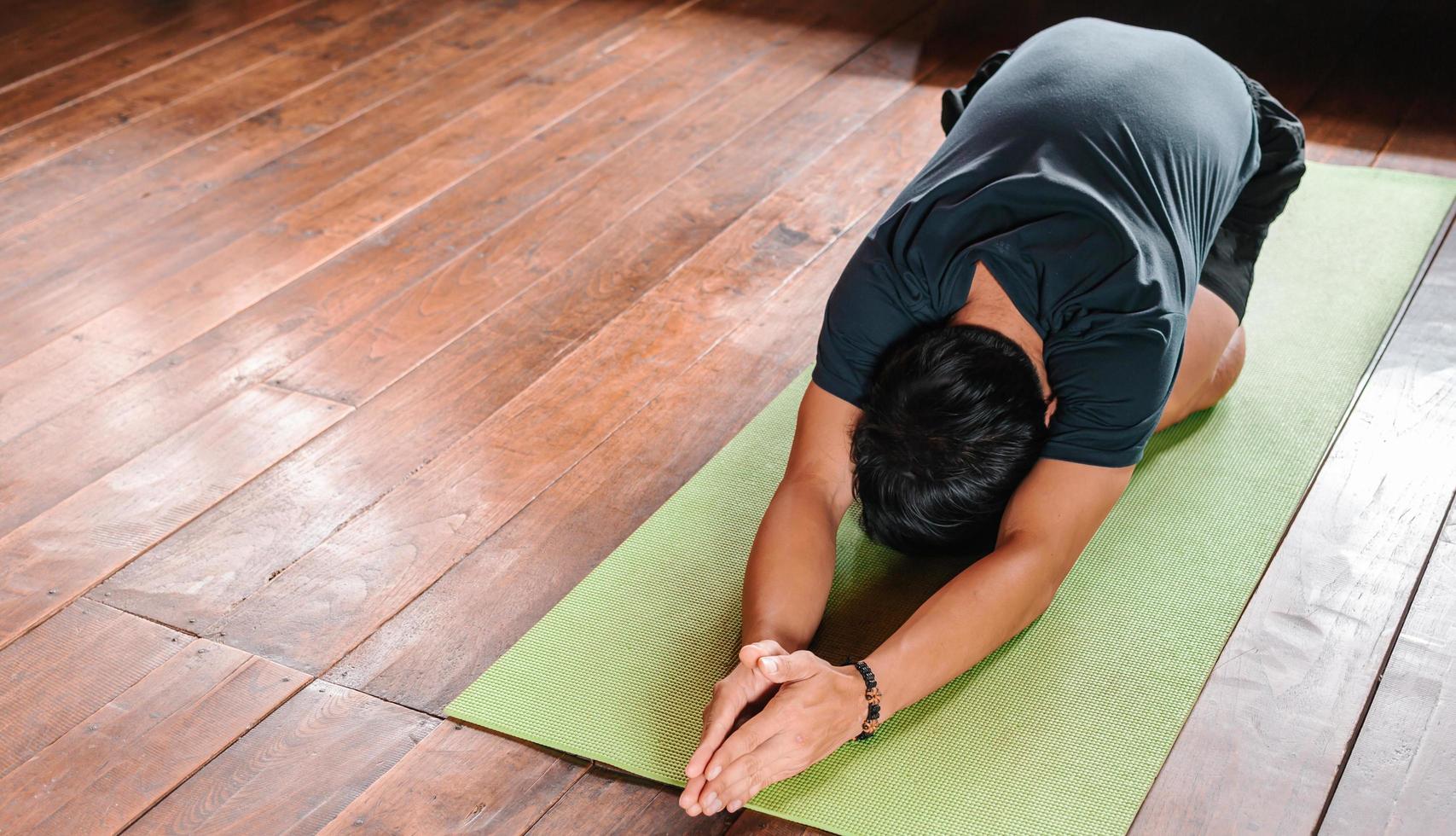 sportlicher asiatischer mann in schwarz macht yoga, während er zu hause auf yogamatte mit holzboden trainiert. mann yoga praxis pose training gesundes lebenskonzept foto