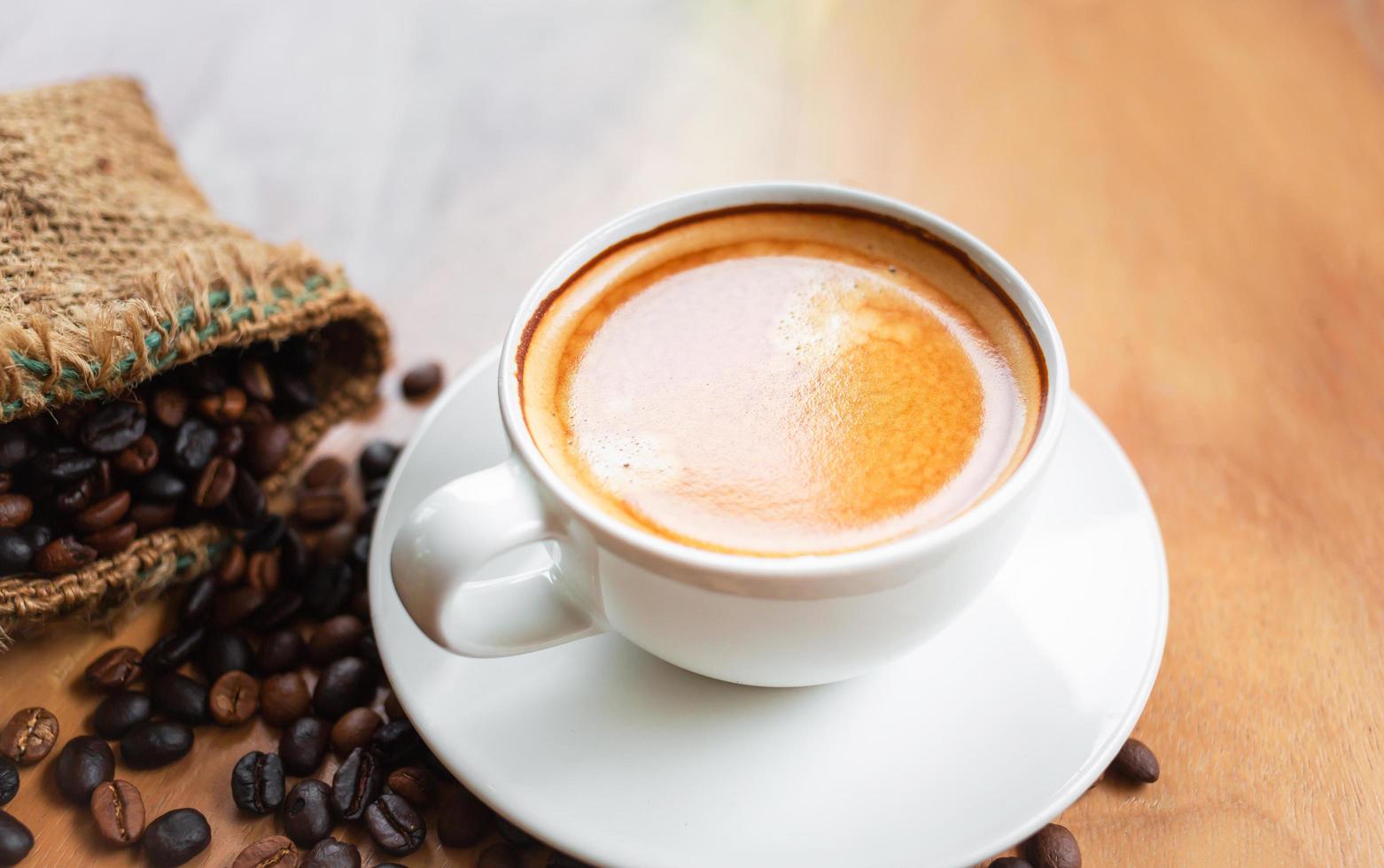 Nahaufnahme einer Tasse Latte mit goldenem Schaum und gemischten oder gemischten Kaffeebohnen in einem braunen Sack auf einem alten Holzboden, Draufsicht. foto