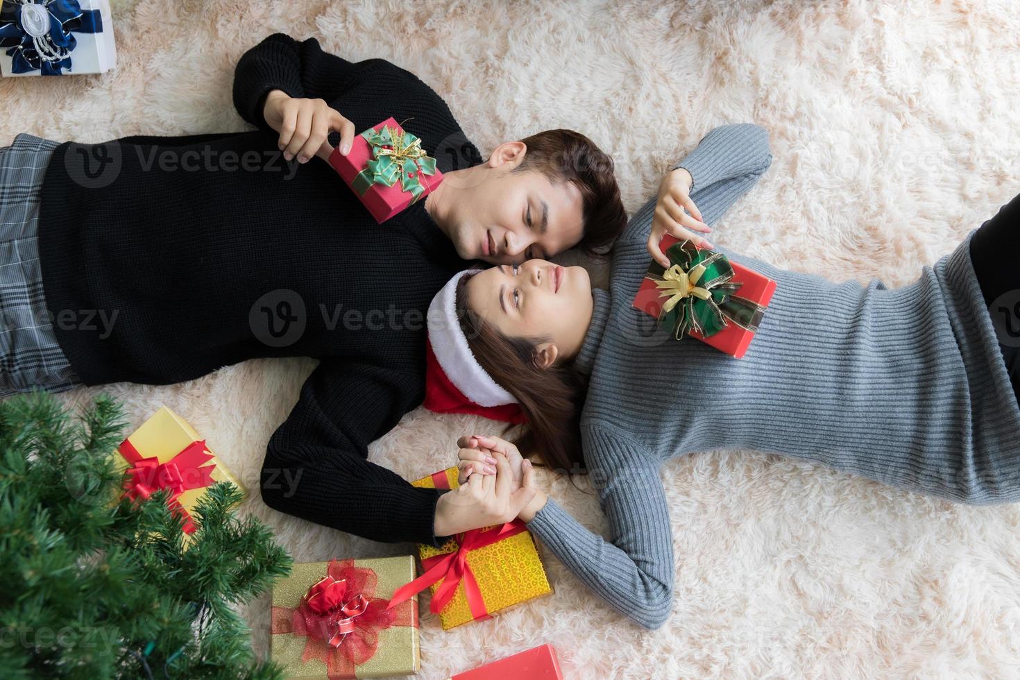 mann und frau liegen auf teppich auf dem boden in weihnachtlich dekoriertem zimmer mit weihnachtsbaum und geschenkbox foto