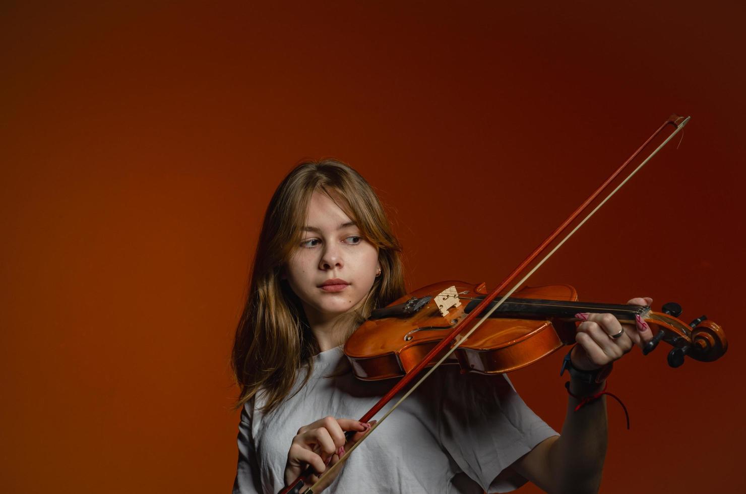 ein Mädchen mit Geige auf dunklem Hintergrund, das ein weißes T-Shirt trägt foto