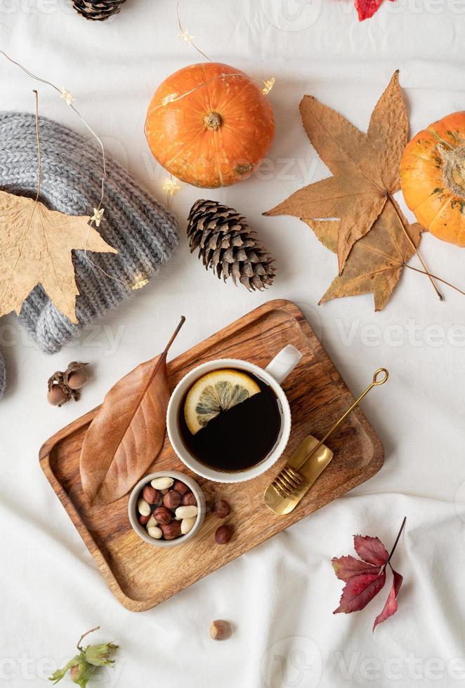 gemütliche Herbstkomposition, Pulloverwetter. heißer tee mit zitrone und nüssen auf holztablett, umgeben von herbstblättern und pullovern, flach gelegt foto