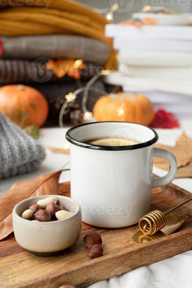 gemütliche Herbstkomposition, Pulloverwetter. heißer tee mit zitrone und nüssen auf holztablett, umgeben von herbstblättern und pullovern, bechermodelldesign foto