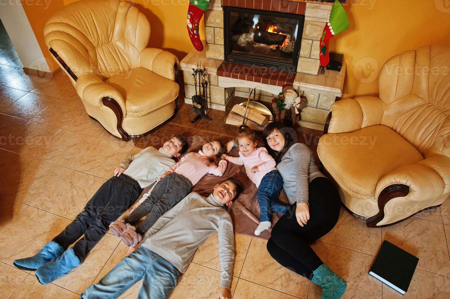 glückliche junge große Familie an einem Kamin im warmen Wohnzimmer am Wintertag. Mutter mit vier Kindern zu Hause. foto