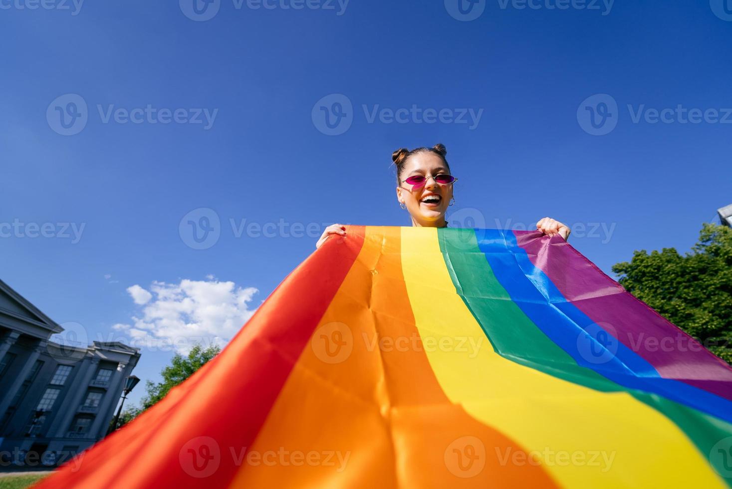 Eine junge Frau entwickelt eine Regenbogenfahne gegen den Himmel foto