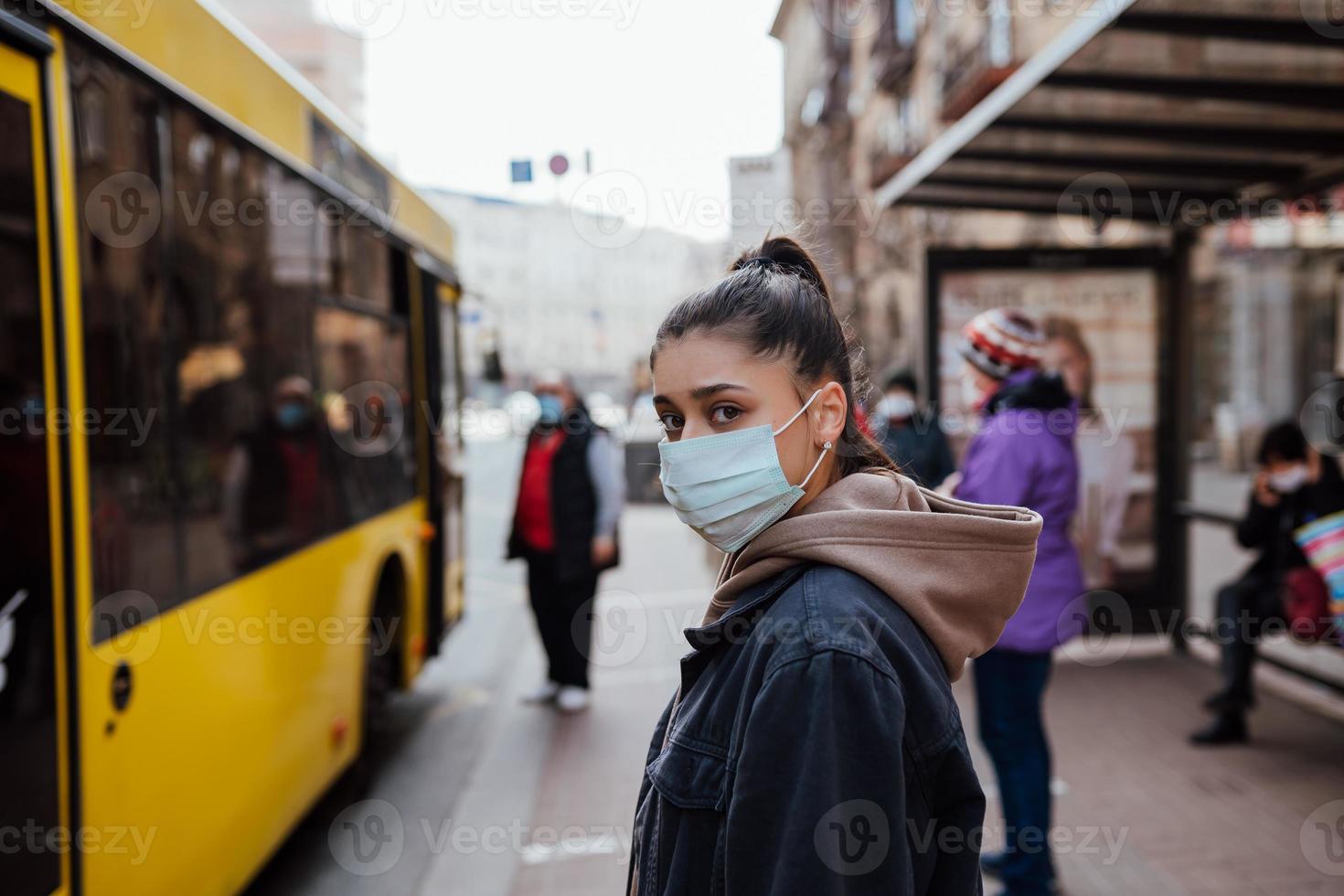 junge Frau mit chirurgischer Maske im Freien an der Bushaltestelle auf der Straße foto