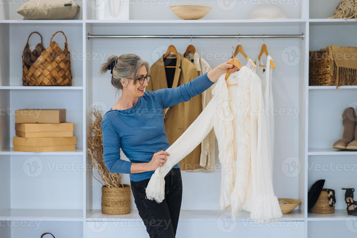 ältere frau während wählt weißen pullover zu hause foto