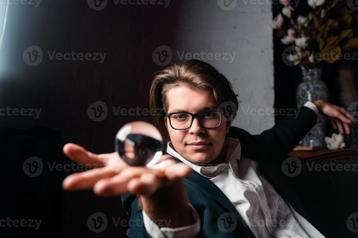 junger Mann, der eine klare, transparente Kristallglaskugel in der Hand hält foto