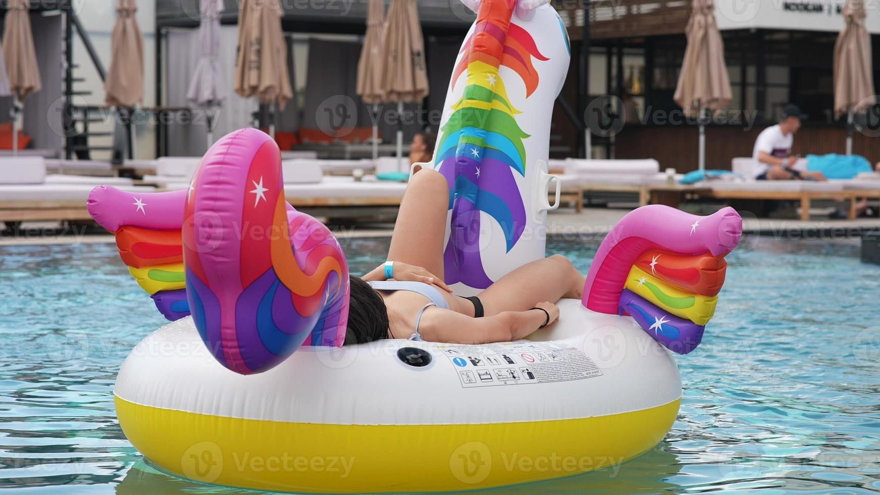 Frau im Bikini in aufblasbarer Einhorn-Spielzeugmatratze schwimmt im Pool. foto