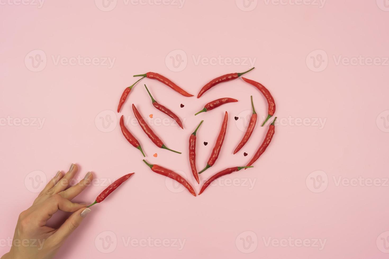 rote scharfe chilischoten in form des herzens liegen auf einem rosa hintergrundtisch foto