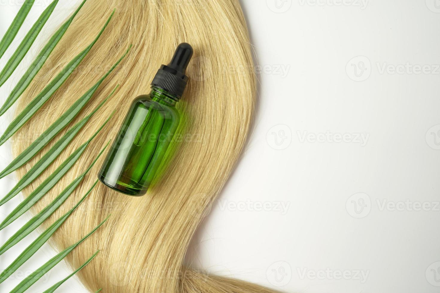 Eine Tropfflasche mit grünem cbd-Öl oder Serum für die Haarpflege in goldenen Kapseln, die auf einer blonden Haarsträhne liegen. haarpflege- und glättungskonzept foto