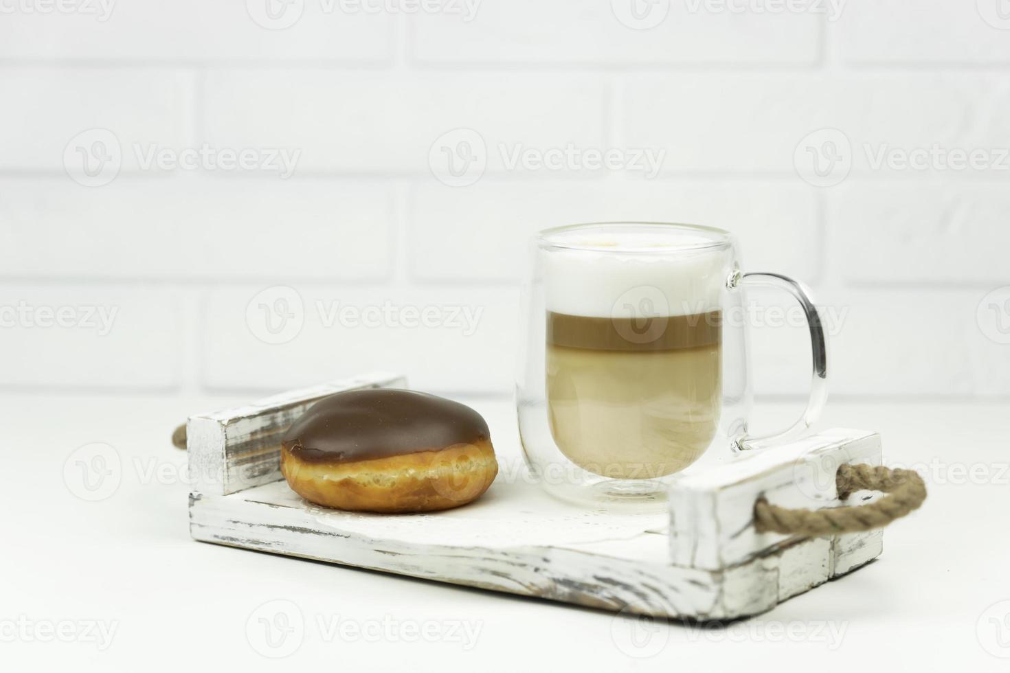 eine tasse latte und ein glasierter donut liegen zum frühen frühstück auf einem holztablett foto