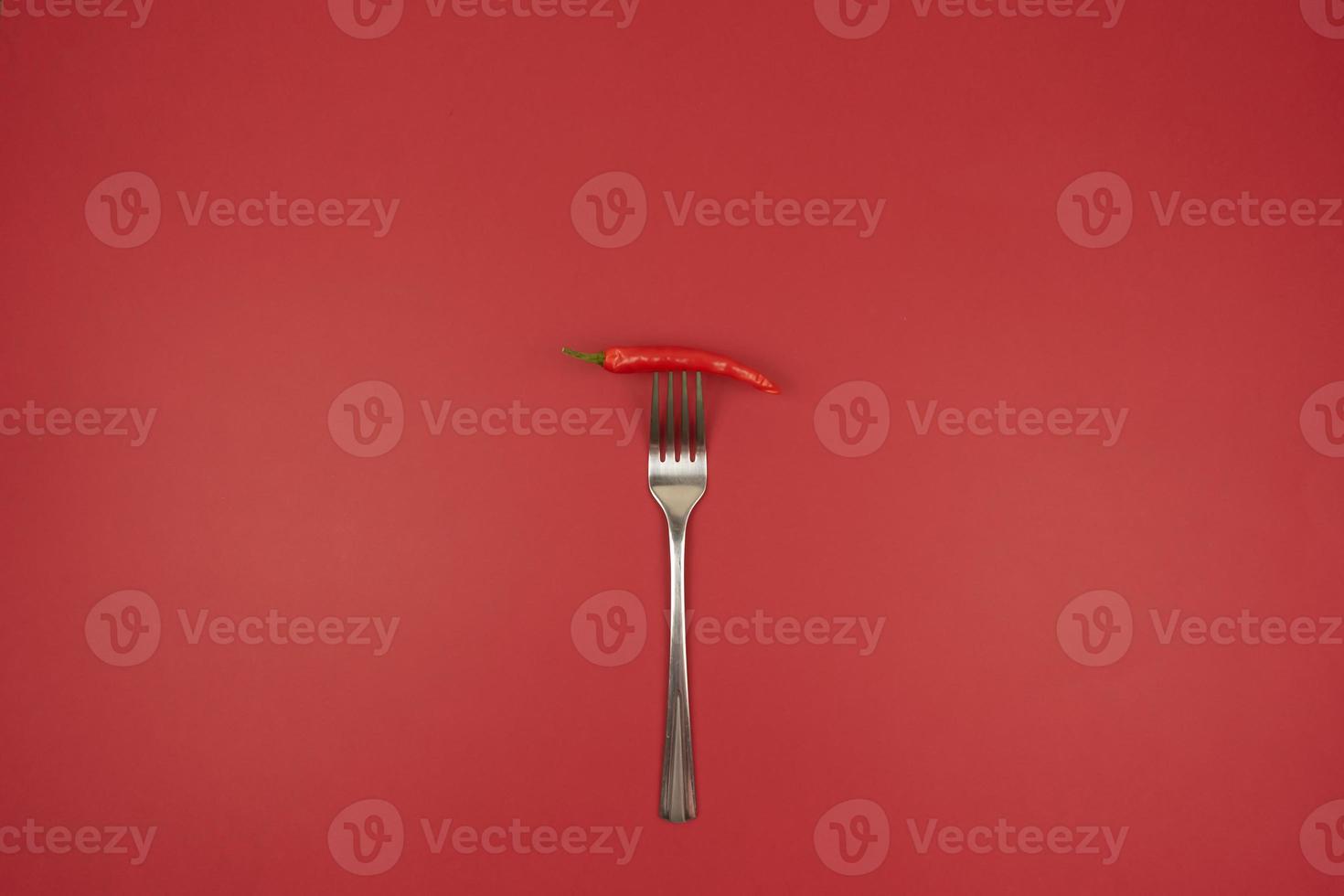 eine rote scharfe Chilischote auf einer Gabel auf rotem Hintergrund foto