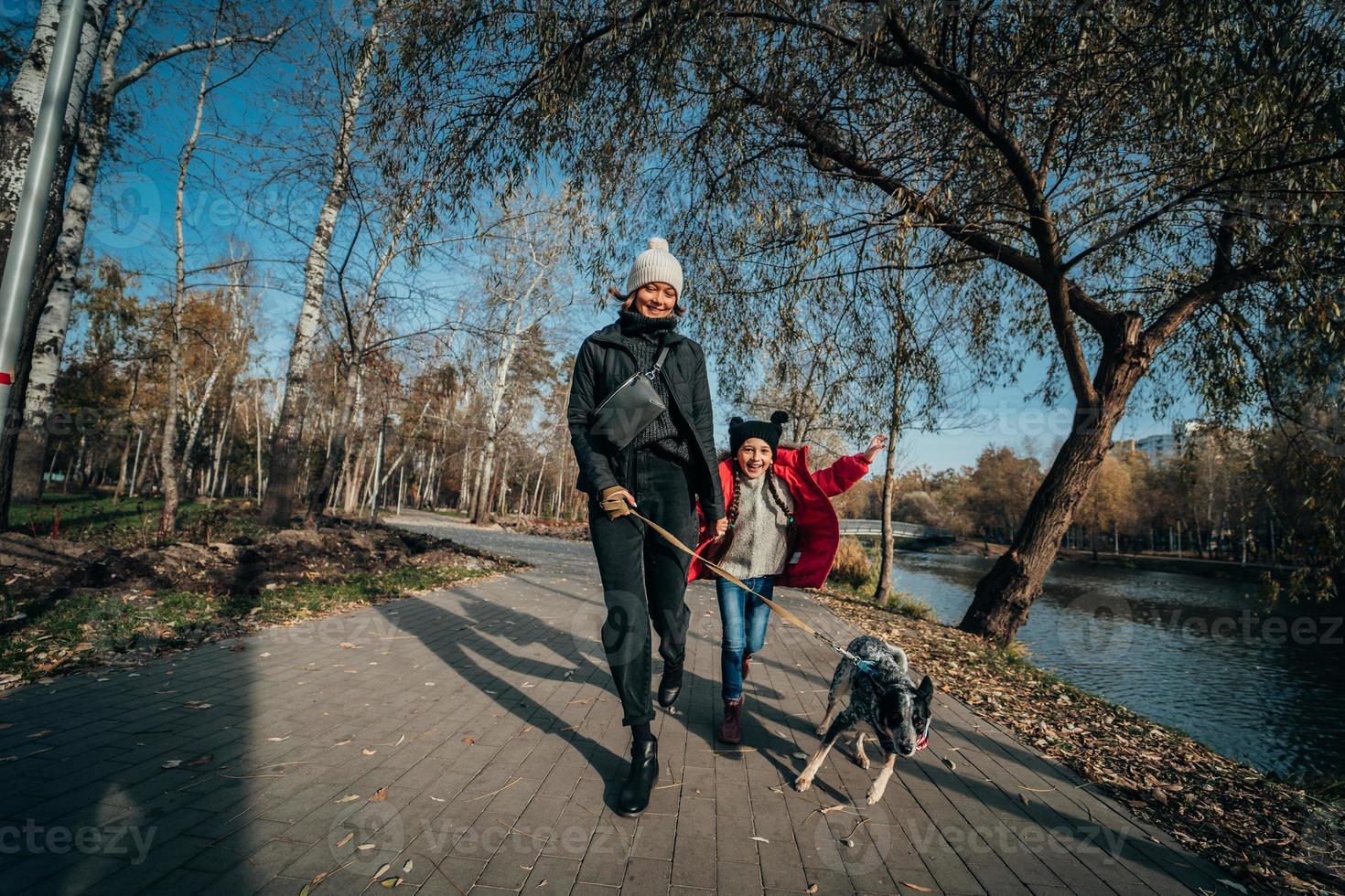 glückliche mutter und ihre tochter gehen mit hund im herbstpark spazieren foto