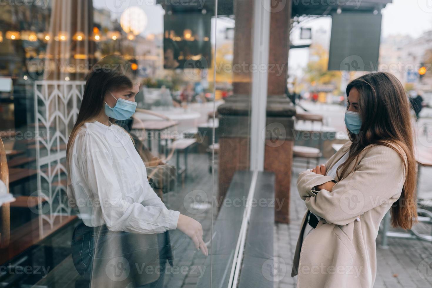 zwei Frauen in Schutzmasken gegenüber, Fenster dazwischen. foto