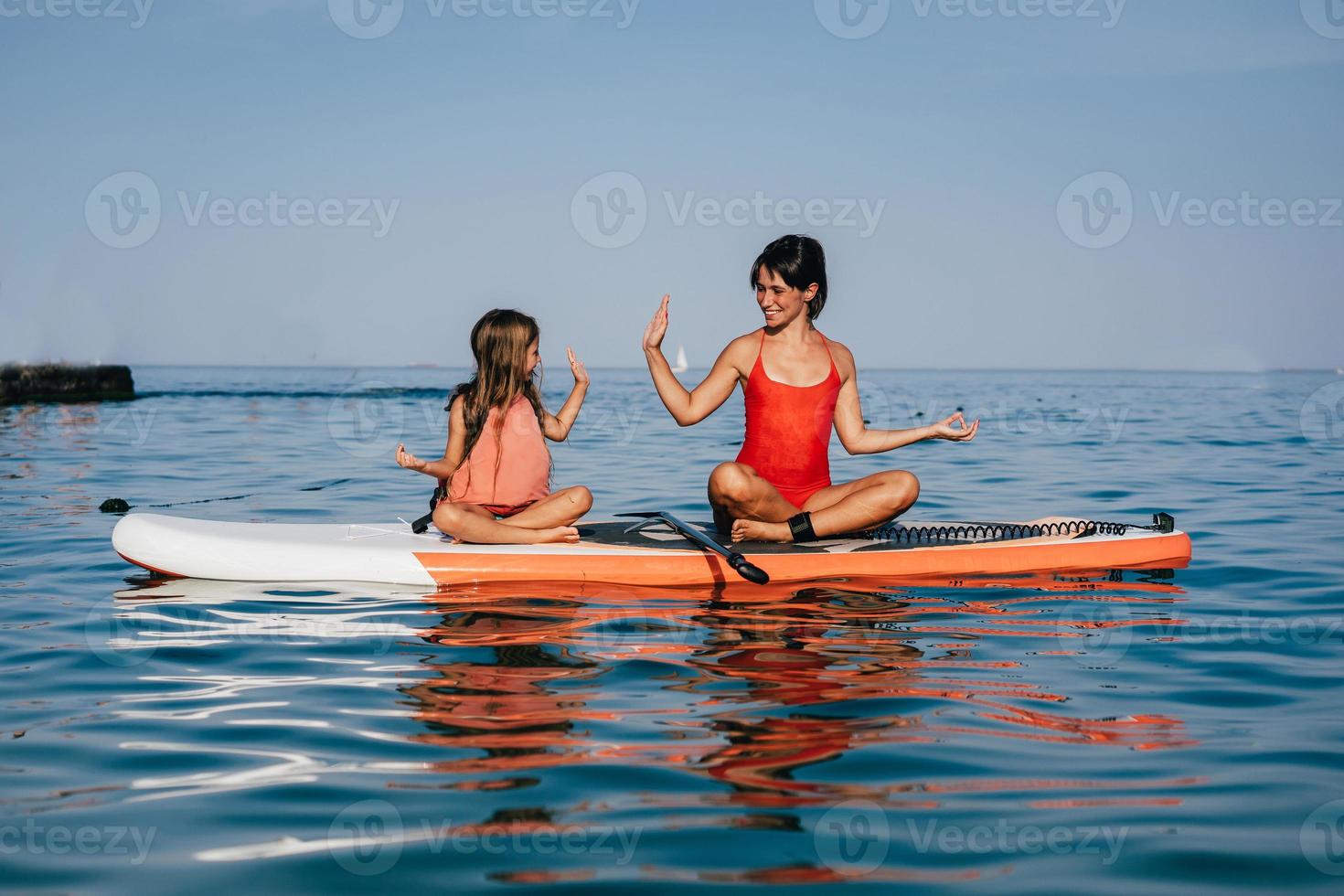 mutter und kleine tochter machen yoga auf dem paddelbrett foto