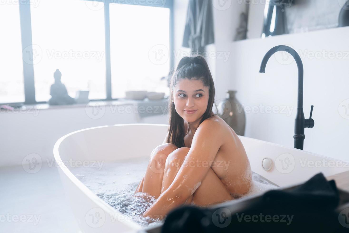 junge Frau umarmt ihre Beine, während sie in der Badewanne sitzt foto