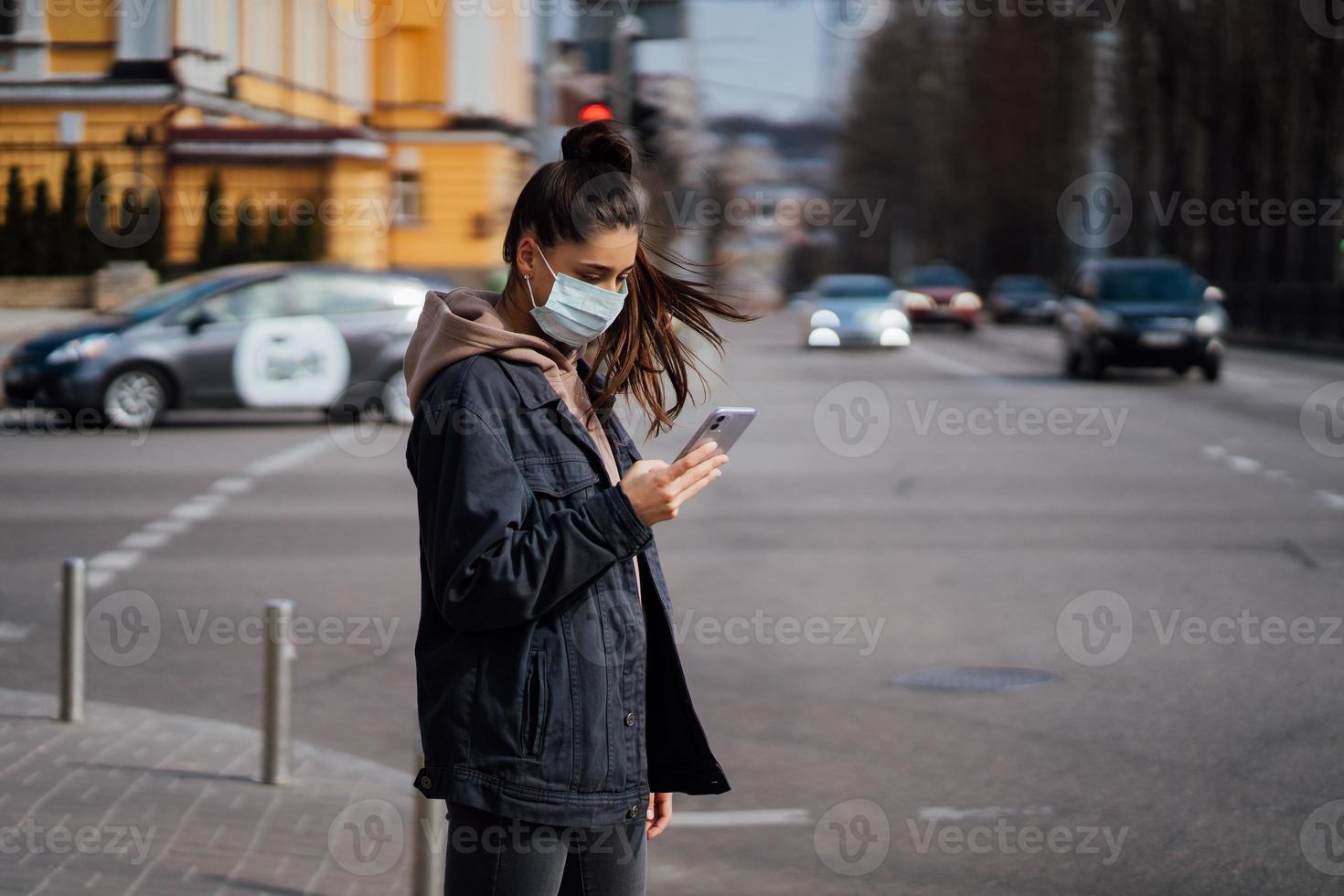 Mädchen in Schutzmaske mit Smartphone im Freien. covid 19. weltweite coronavirus-pandemie. foto