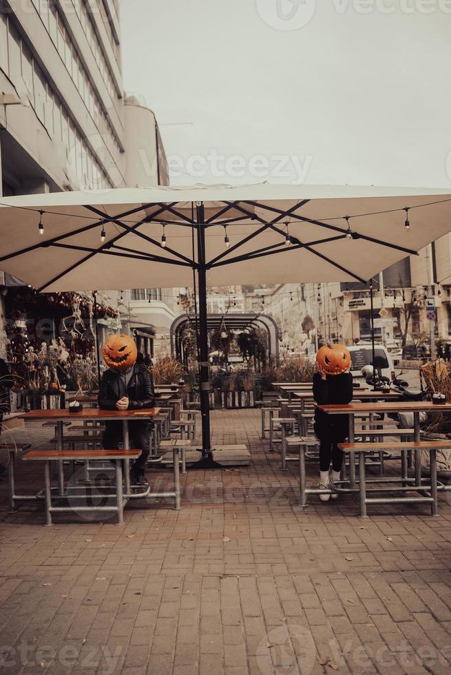 Mann und Mädchen mit Kürbisköpfen in einem Straßencafé foto