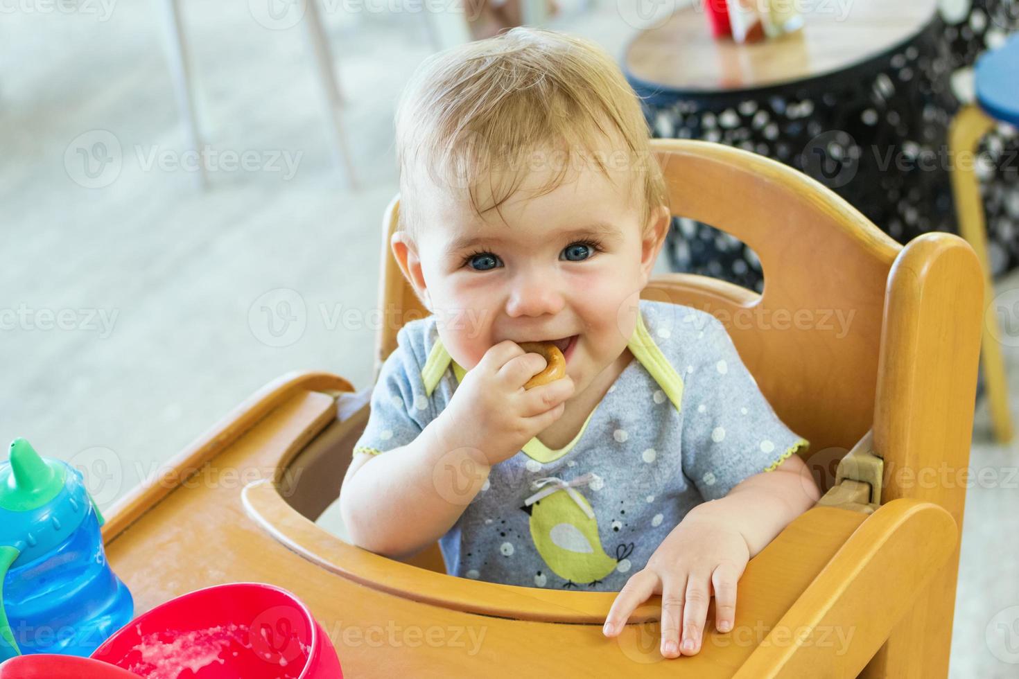 Das entzückende kleine Mädchen sitzt nach dem Mittagessen in einem hölzernen Kinderstuhl und isst Kekse. foto