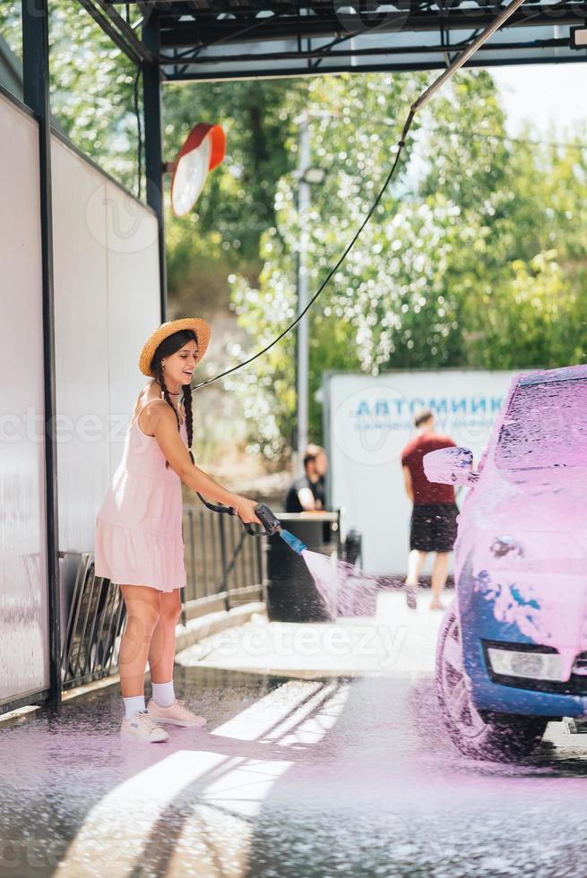 Brünette aus einem Hochdruckschlauch trägt einen Reiniger auf das Auto auf foto