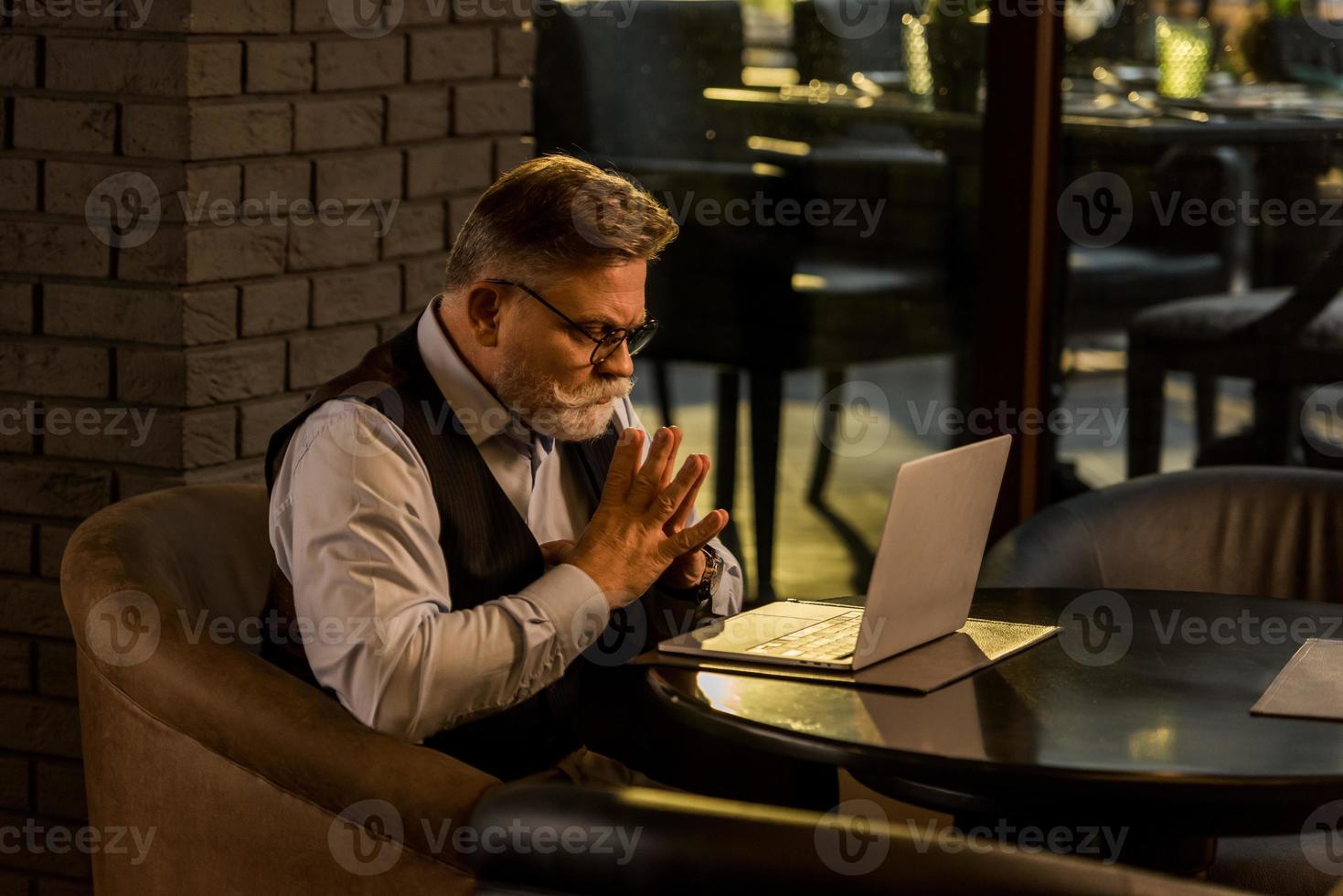 Seitenansicht des nachdenklichen älteren Geschäftsmannes, der Laptop-Bildschirm im Café betrachtet foto