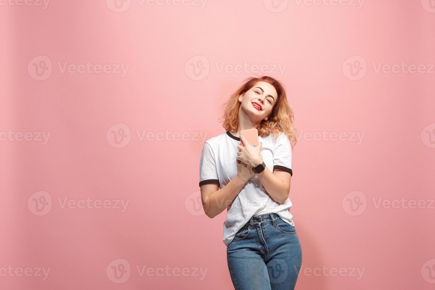 Die glückliche Geschäftsfrau lächelt und hält das Smartphone vor rosa Hintergrund in der Hand foto