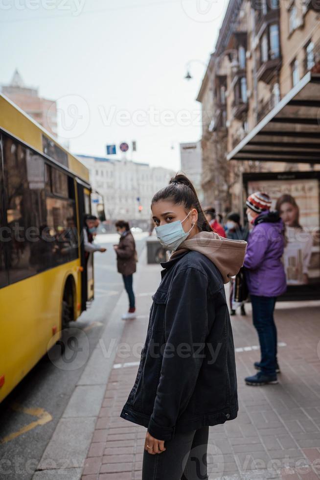 junge Frau mit chirurgischer Maske im Freien an der Bushaltestelle auf der Straße foto