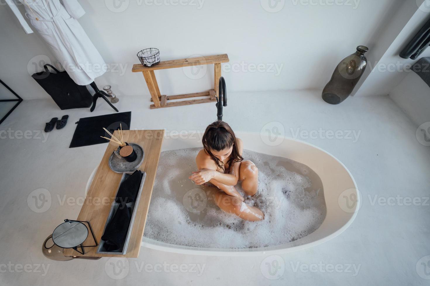 junge Frau umarmt ihre Beine, während sie in der Badewanne sitzt foto