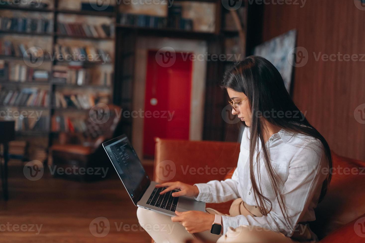 junge Frau sitzt auf einem roten Sofa, während sie an einem Laptop arbeitet. foto