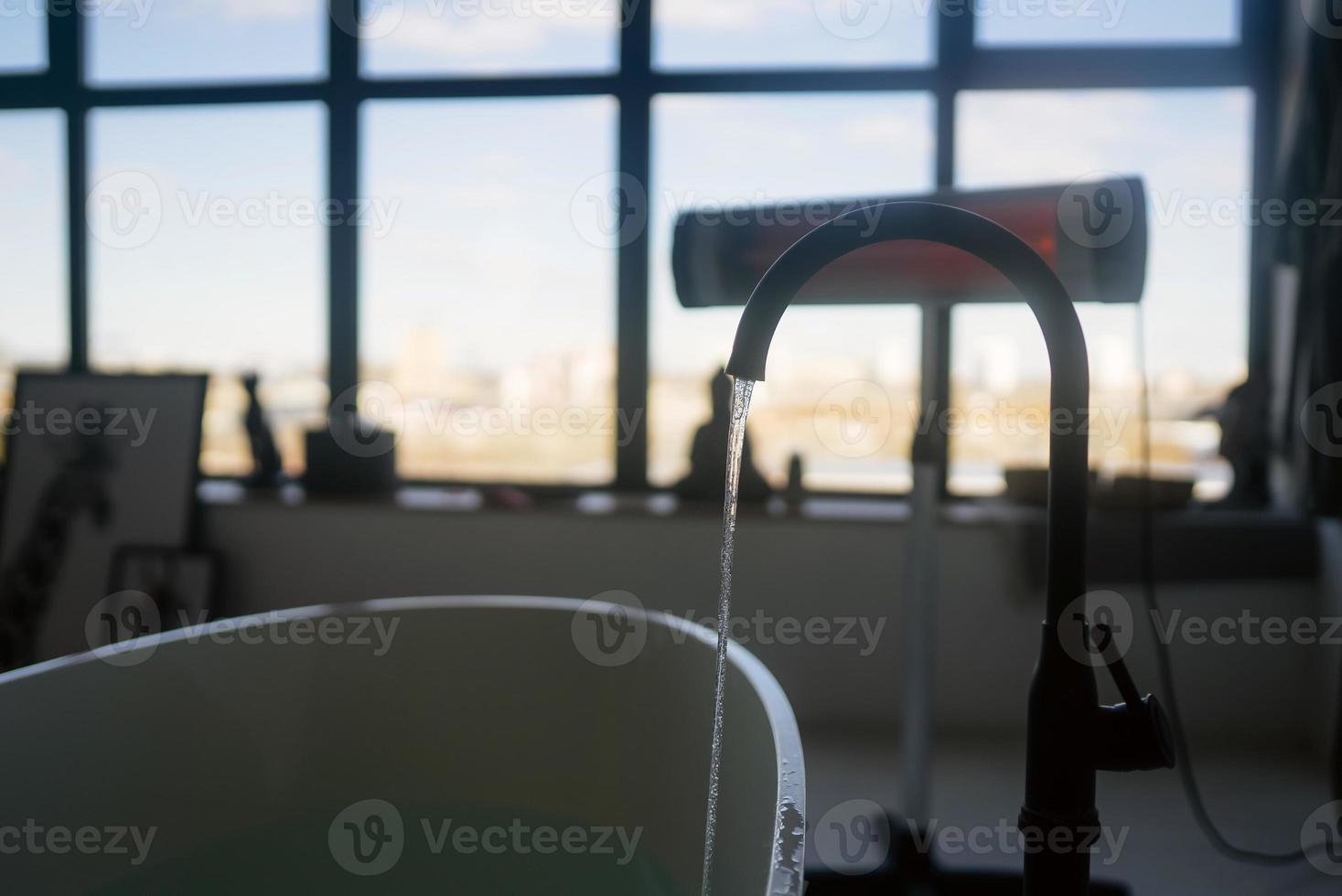 Wasser fließt aus einem luxuriösen Wasserhahn in eine große moderne Badewanne foto