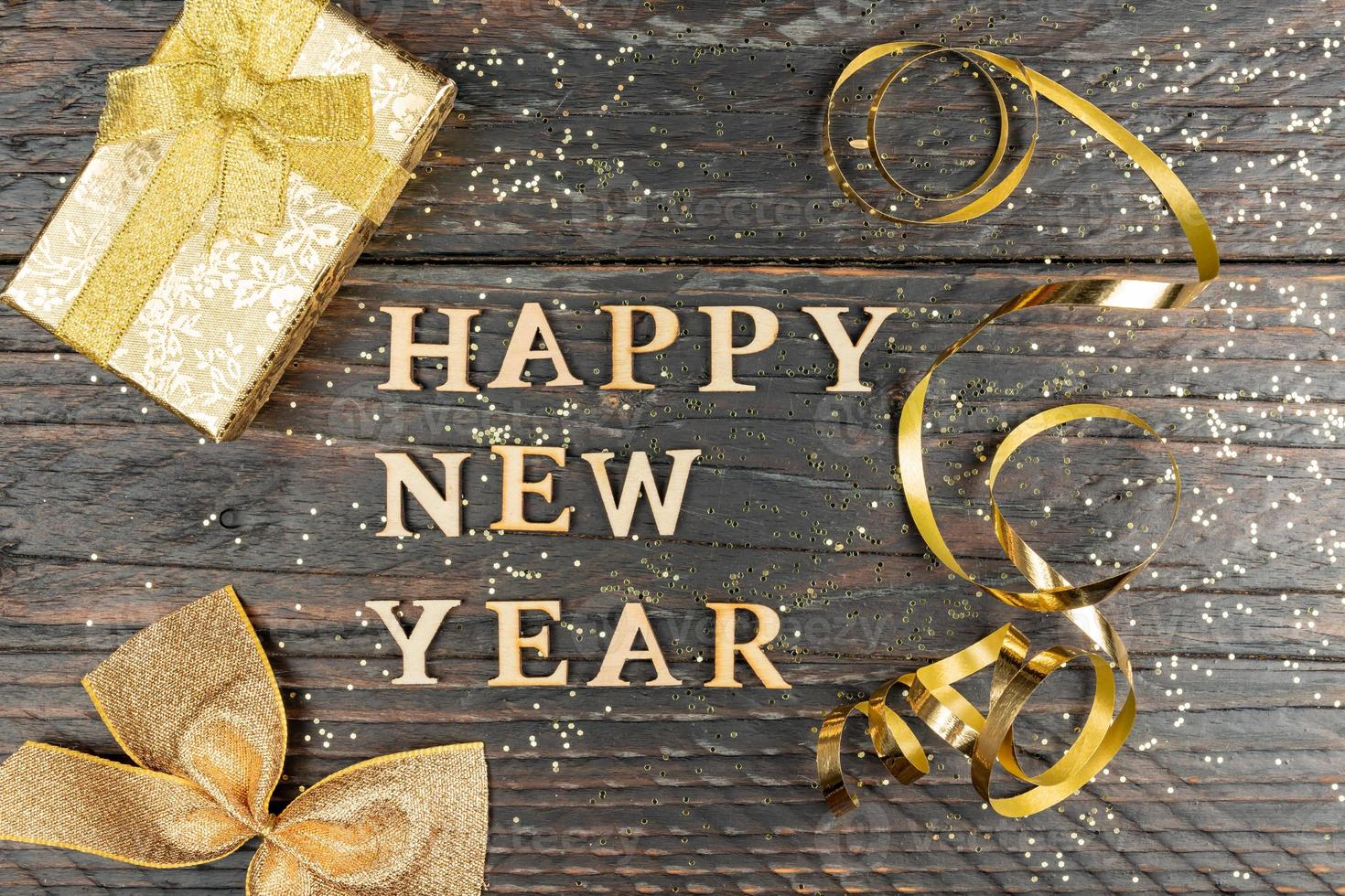 festliche grußkarte mit frohem neujahrstext auf holzboden mit goldfunkelndem konfetti und geschenkbox foto