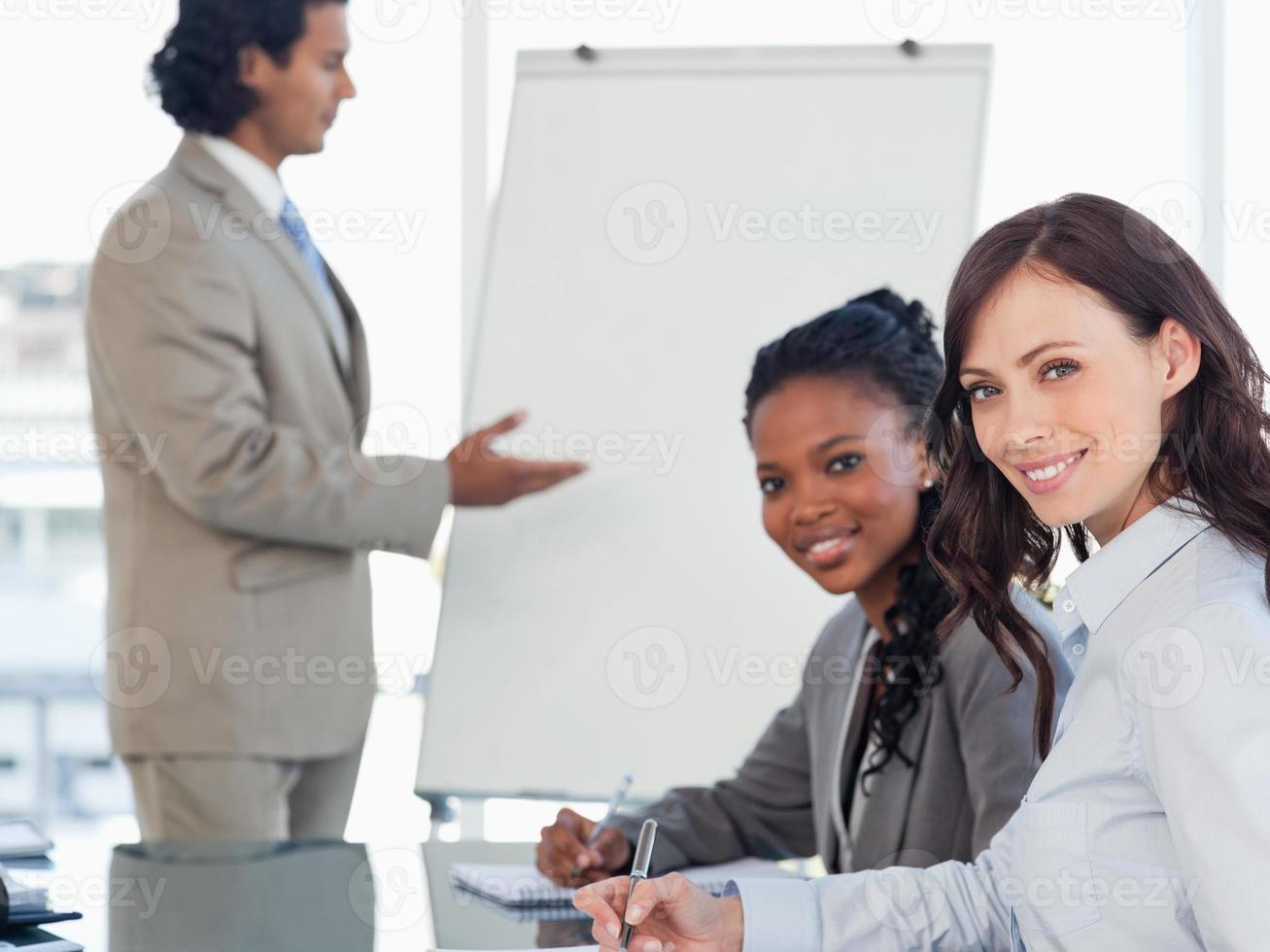 zwei junge lächelnde Angestellte, die arbeiten, während sie einer Präsentation zuhören foto