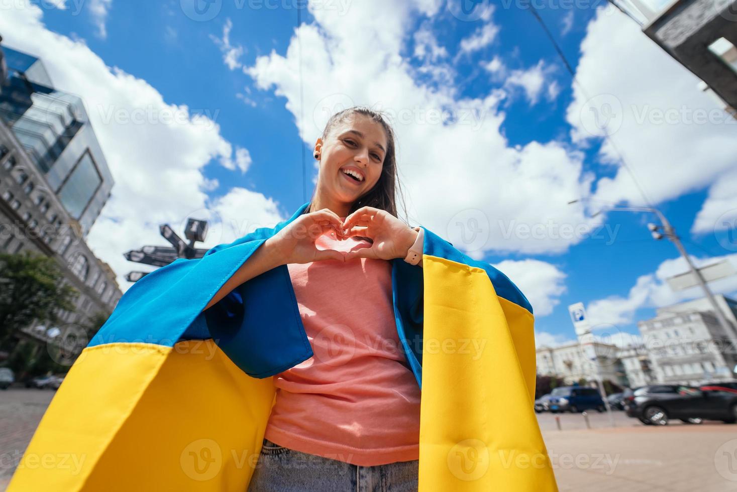 junge Frau mit ukrainischer Flagge zeigt Herz mit Händen foto