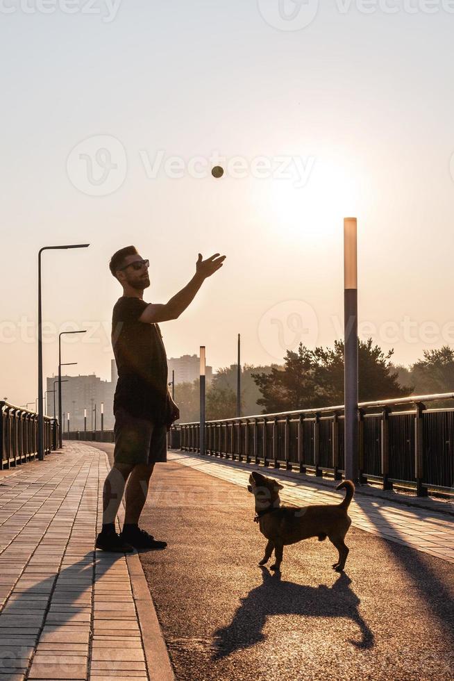 Der junge Mann spielt morgens mit seinem Hund auf einer leeren Straße. foto