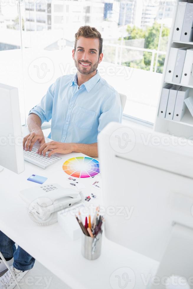 lächelnder männlicher Bildbearbeiter unter Verwendung des Computers foto